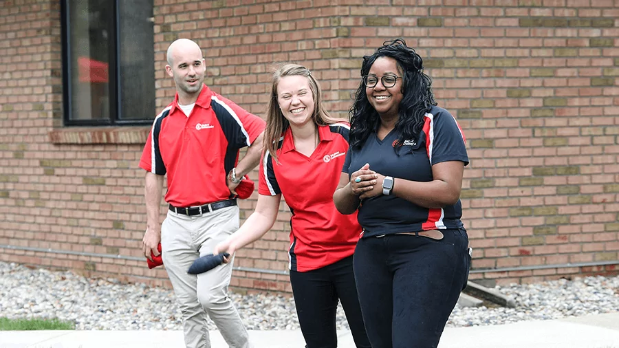 Three students in red and black Baker shirts smile while walking outside of a campus building.