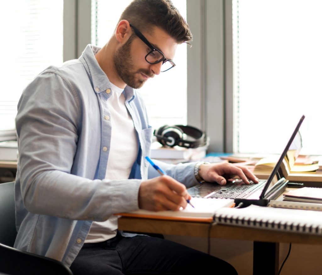 Adult male at a computer taking notes.