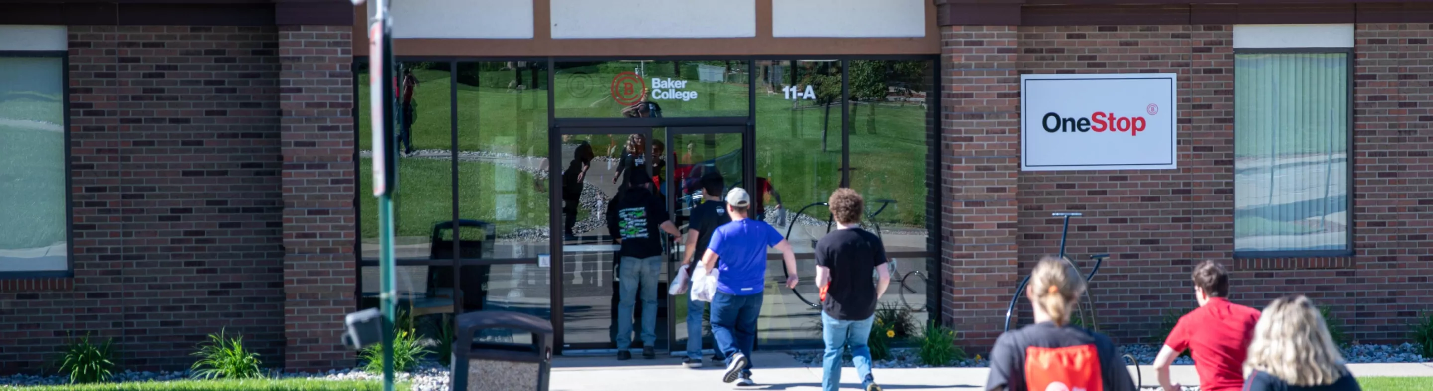 Students enter a campus building with a OneStop sign hanging out front.