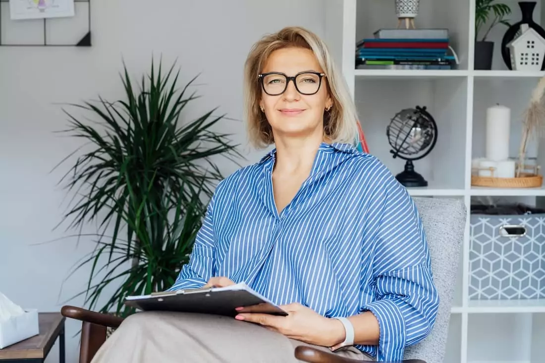 Female Psychologist Smiling Sitting On Armchair In Office.